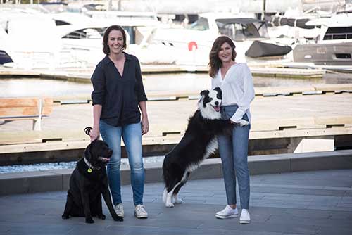 PetWell owners Tracey & Ayda with a black labrador and border collie in a boat harbour